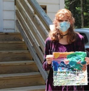 a woman standing outside holding a quilte piece of art a child made